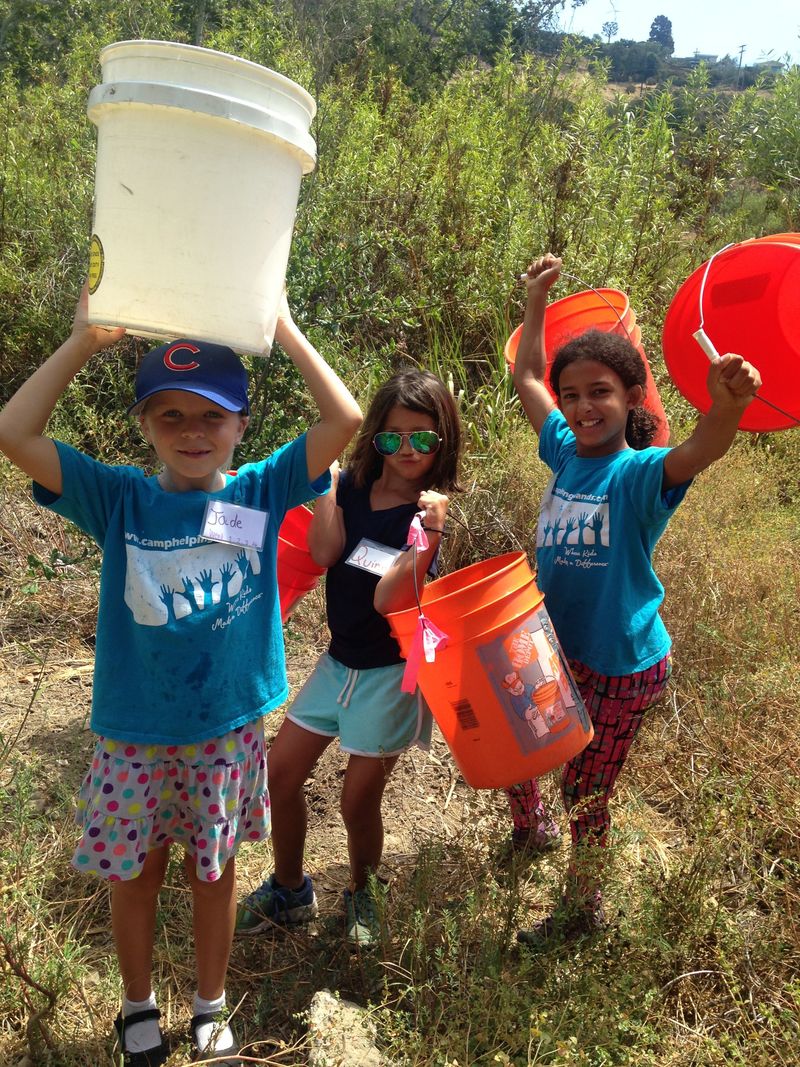 Three campers at Camp Helping Hands wearing camp t-shirts and carrying colorful water buckets while on a hike.