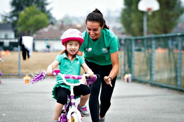 Female camp counselor at Pedelheads Bike Camp in Los Angeles teaching a young camper how to ride a bike.