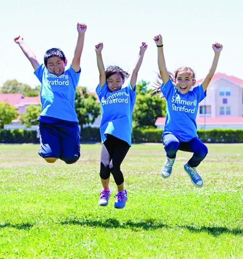 Three kids jumping for joy on a grass ball field at Summer at Stratford Day Camp